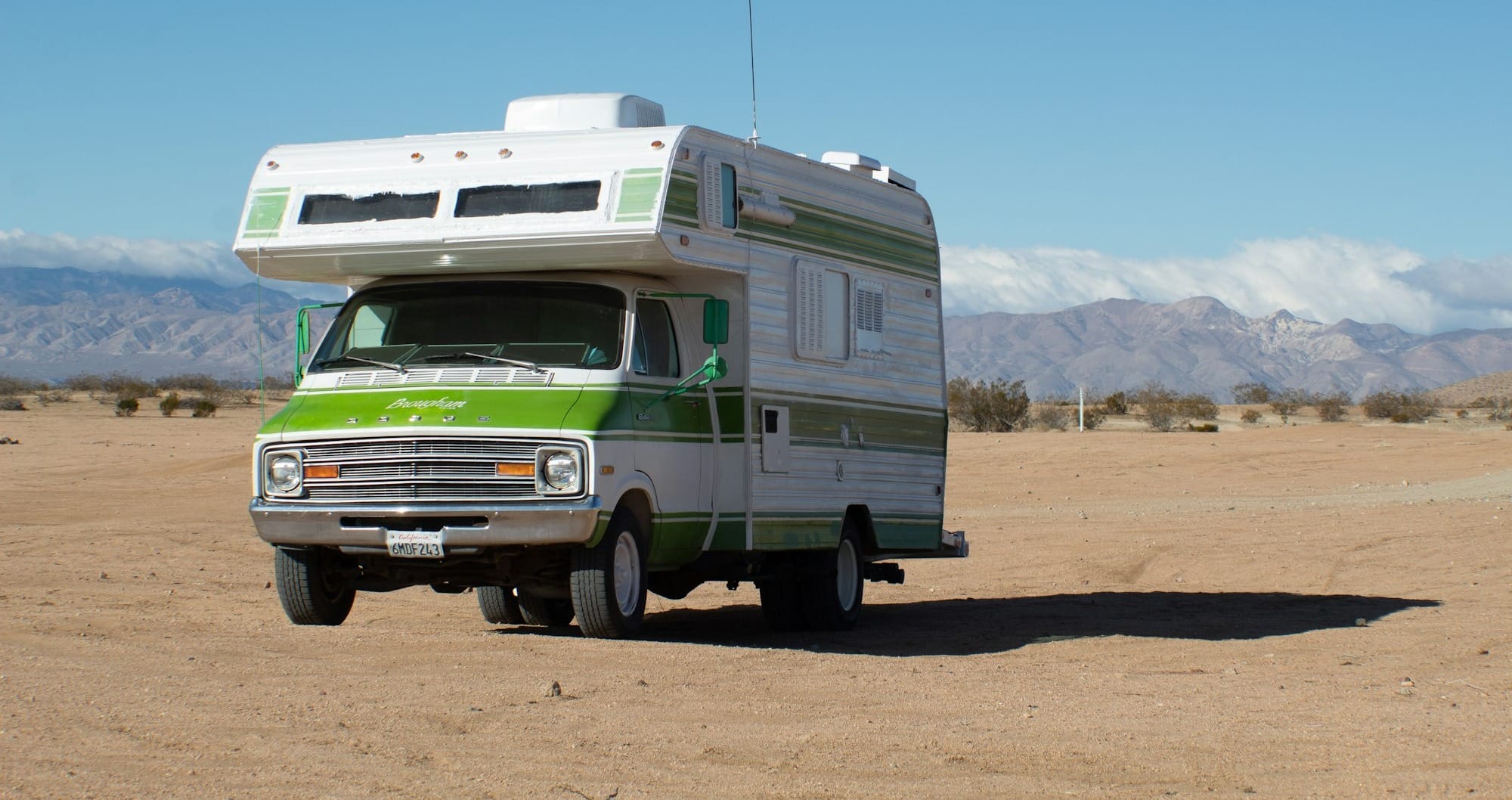 white and green rv on brown field under blue sky during daytime